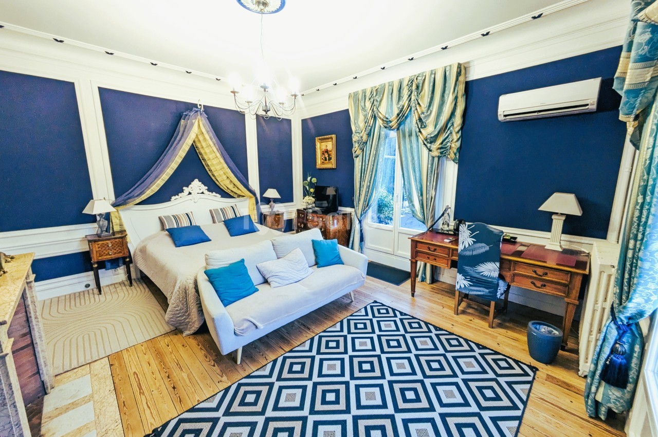 Chambre élégante avec murs bleus, lit double, mobilier en bois, tapis géométrique et fenêtre avec rideaux.