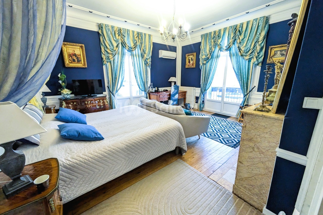 Chambre élégante avec murs bleus, lit double, rideaux assortis, cheminée en marbre et mobilier classique.