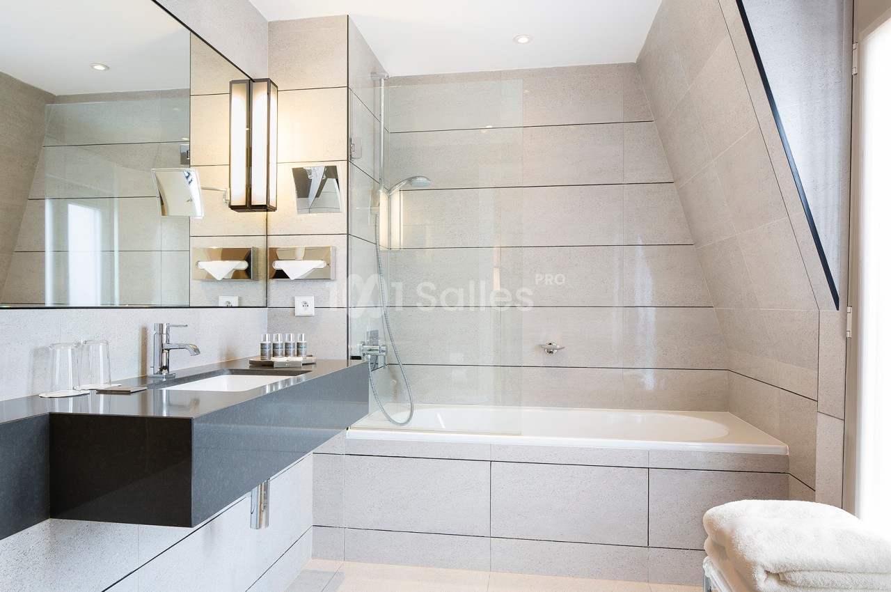 Salle de bain moderne avec baignoire, douche vitrée, lavabo noir, grand miroir et éclairage intégré.