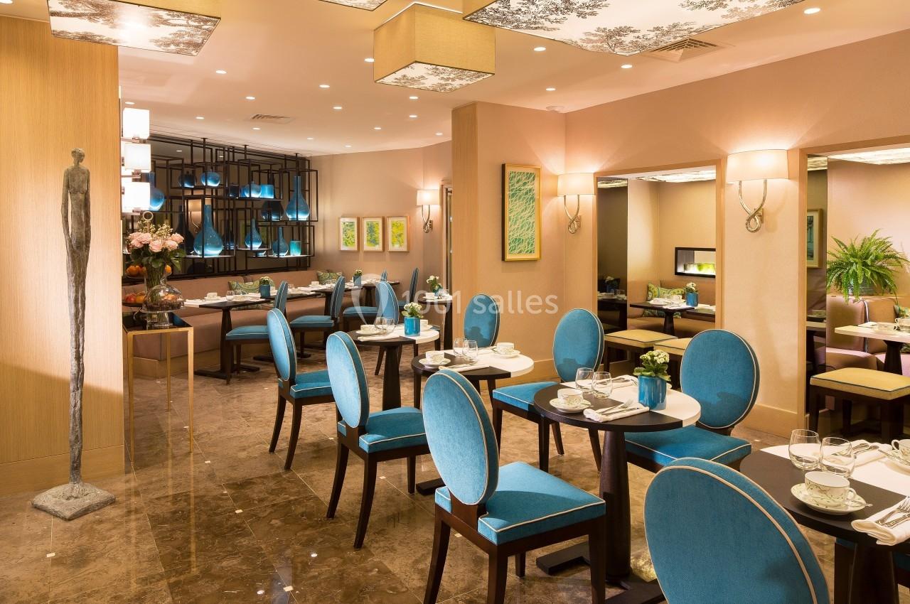 Salle de restaurant élégante avec des chaises bleu turquoise, des tables dressées et un éclairage chaleureux.