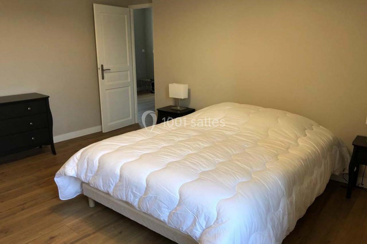 Chambre avec un lit double couvert d'une couette blanche, parquet au sol, murs beiges et mobilier sombre.