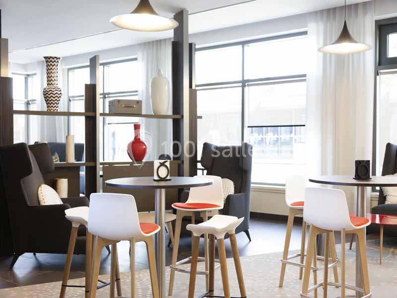 Salle lumineuse avec des tables hautes, des chaises modernes et des fauteuils, décorée de vases sur des étagères.