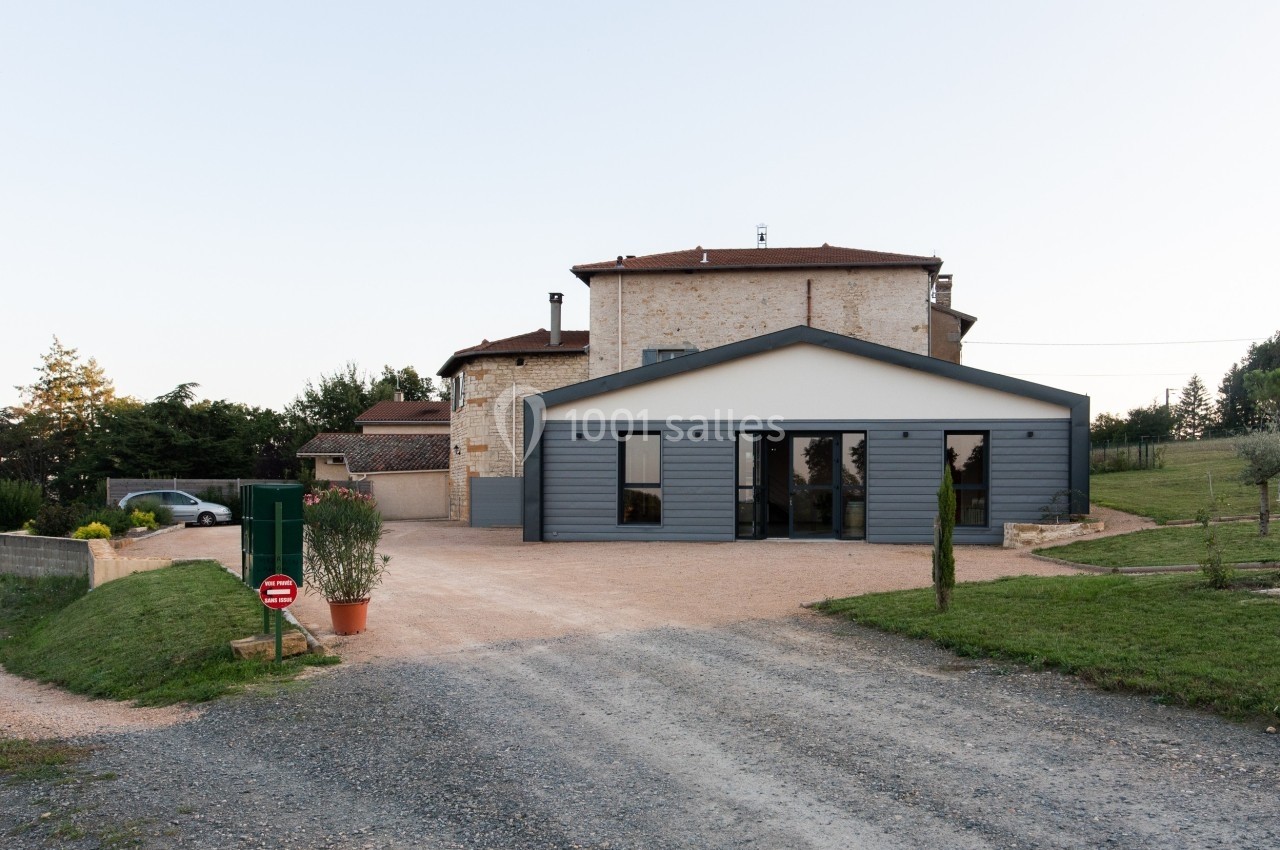 Bâtiment en pierre avec une extension moderne, entouré de pelouse et d'une allée en gravier.