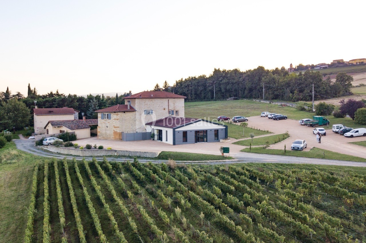 Vue aérienne d'un domaine viticole avec bâtiments en pierre, vignes au premier plan et voitures stationnées.