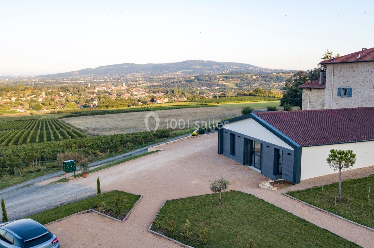 Vue aérienne d'un bâtiment moderne entouré de vignes et de champs, avec des collines en arrière-plan.
