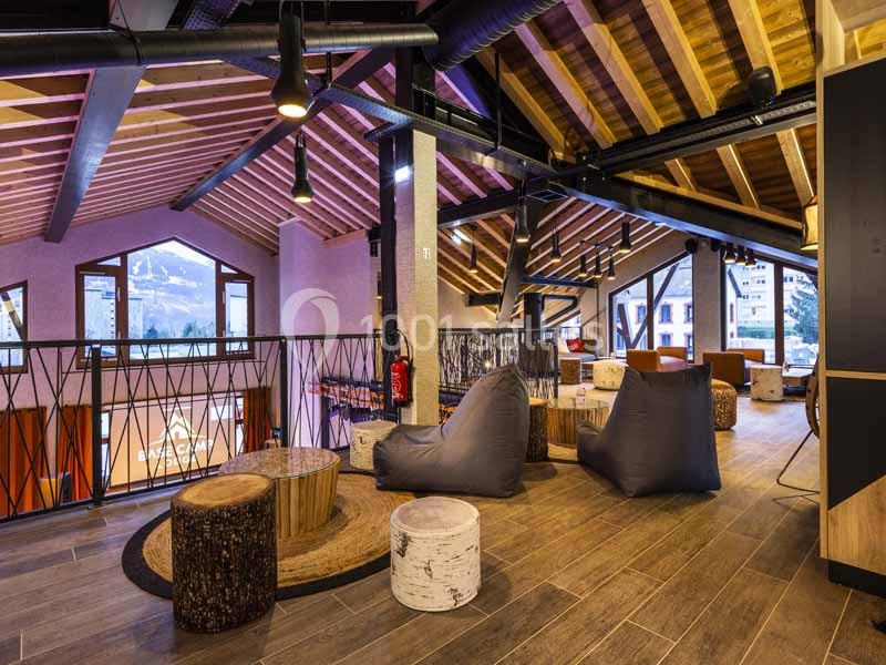 Espace intérieur avec poutres apparentes, fauteuils confortables et vue sur des montagnes à travers de grandes fenêtres.