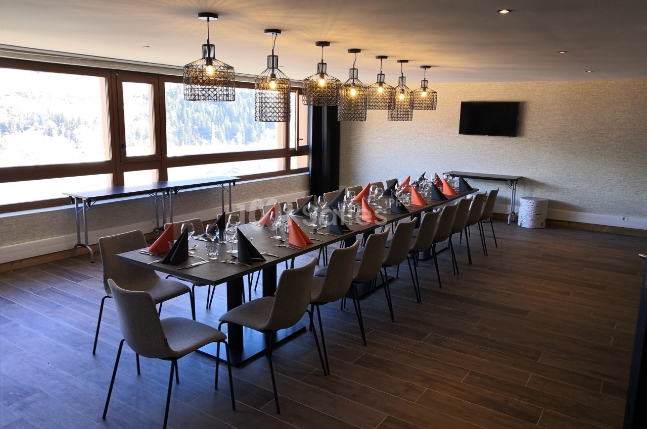 Salle de réunion lumineuse avec une grande table dressée, chaises, lustres modernes et vue sur l'extérieur.