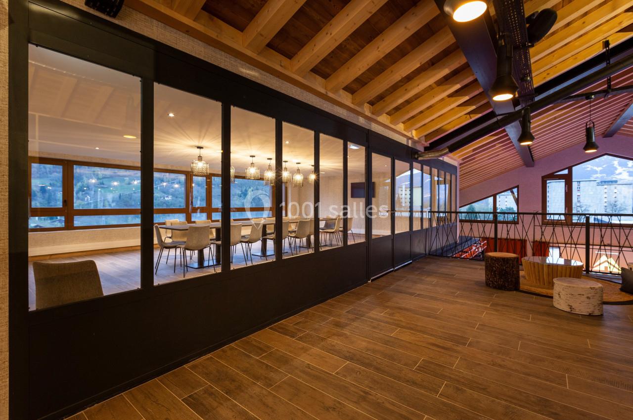 Salle de réunion vitrée avec vue sur des montagnes enneigées, éclairée par des suspensions modernes et un plafond en bois.