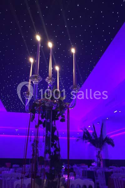 Location salle Le Raincy (Seine-Saint-Denis) - Le Chalet des Pins #13 Lustre à bougies allumées dans une salle éclairée en violet, avec plafond étoilé et décorations végétales.