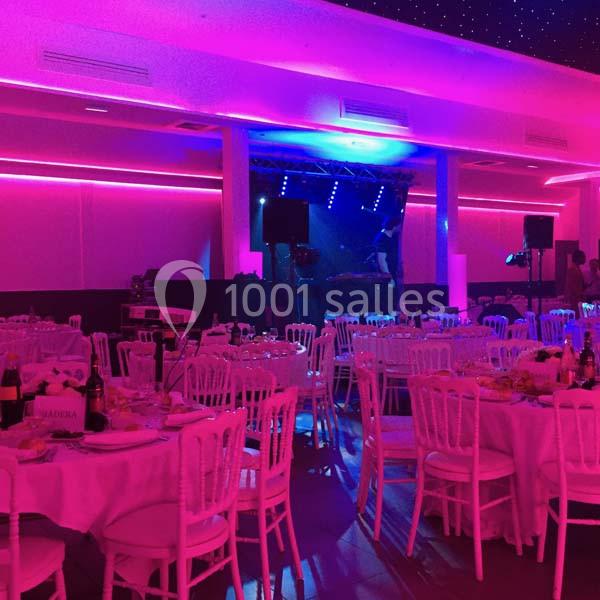 Location salle Le Raincy (Seine-Saint-Denis) - Le Chalet des Pins #7 Salle de réception éclairée de lumières roses et violettes, tables dressées avec chaises blanches.