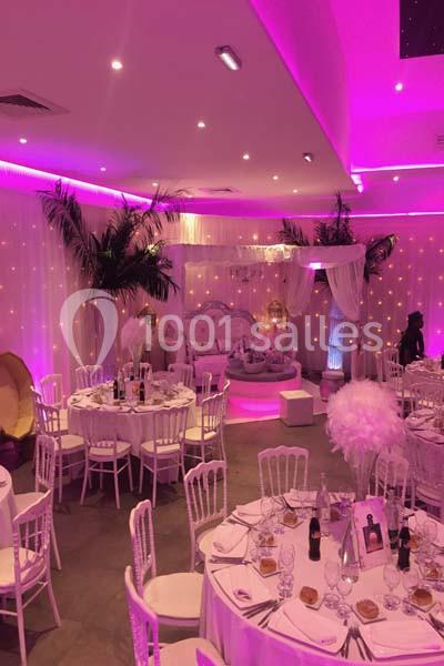 Location salle Le Raincy (Seine-Saint-Denis) - Le Chalet des Pins #5 Salle de réception décorée avec des tables rondes, des chaises blanches, des lumières roses et des éléments décoratifs…