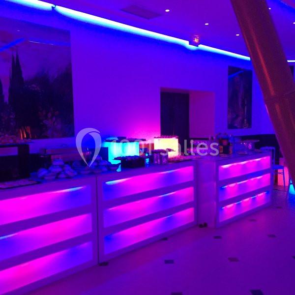 Location salle Le Raincy (Seine-Saint-Denis) - Le Chalet des Pins #18 Comptoirs lumineux violets et bleus dans une salle de réception, avec des boissons et des plats disposés.