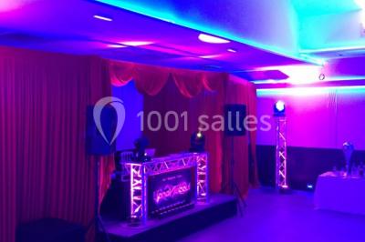 Miniature Location salle Le Raincy (Seine-Saint-Denis) - Le Chalet des Pins #22 Scène de DJ éclairée par des lumières colorées, entourée de rideaux rouges et de haut-parleurs dans une salle.