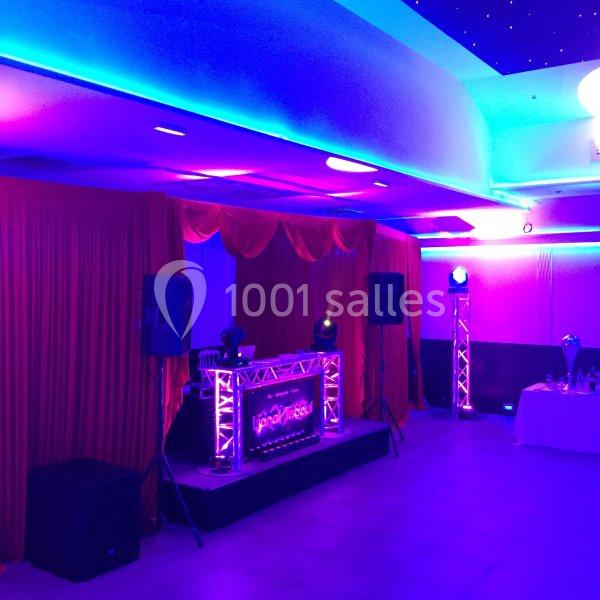 Location salle Le Raincy (Seine-Saint-Denis) - Le Chalet des Pins #22 Scène de DJ éclairée par des lumières colorées, entourée de rideaux rouges et de haut-parleurs dans une salle.