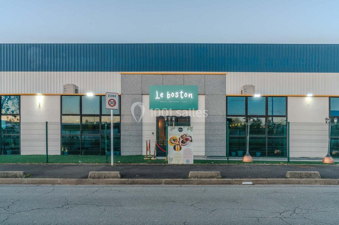 Façade d'un restaurant avec enseigne ’Le Boston’, grandes fenêtres et entrée principale entourée d'une clôture.