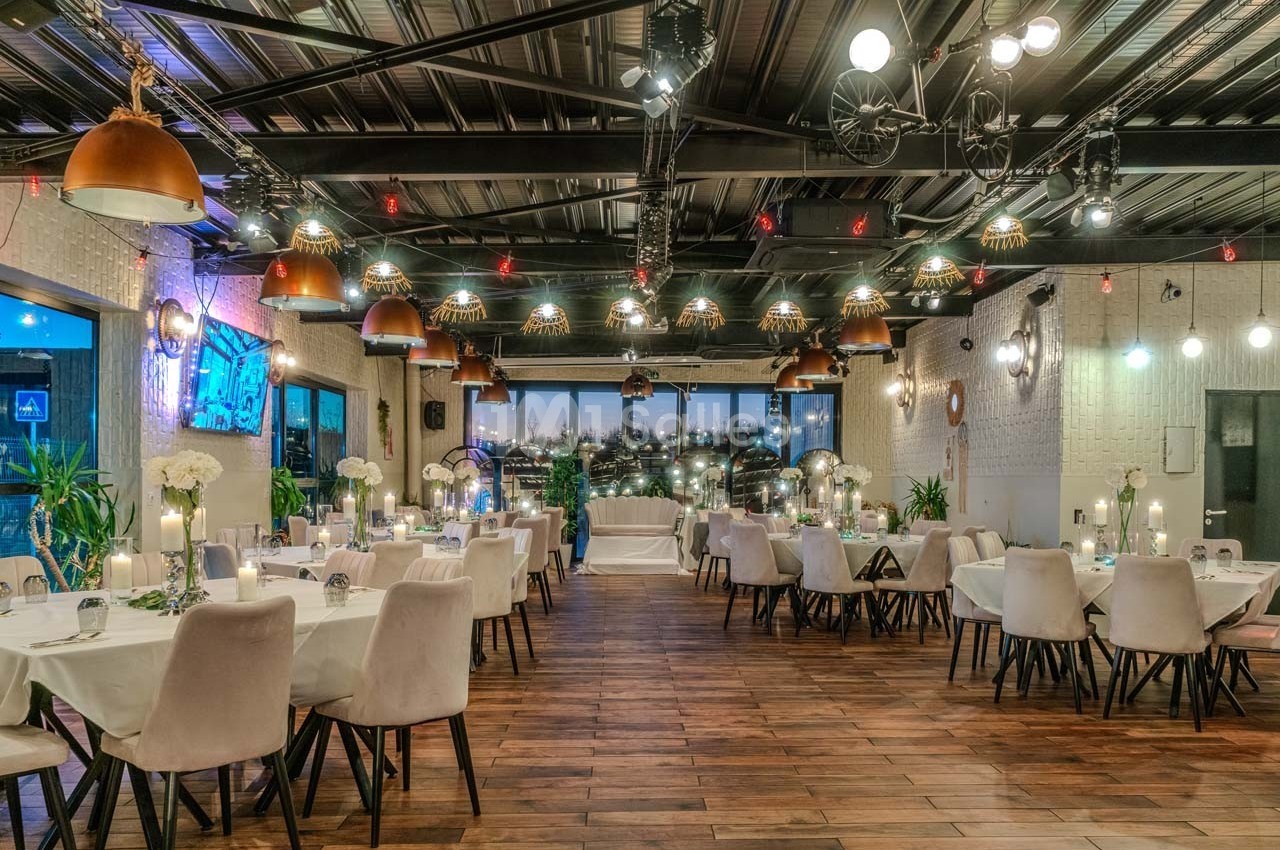 Salle de réception élégante avec tables dressées, éclairage chaleureux et vue sur une ville illuminée en arrière-plan.