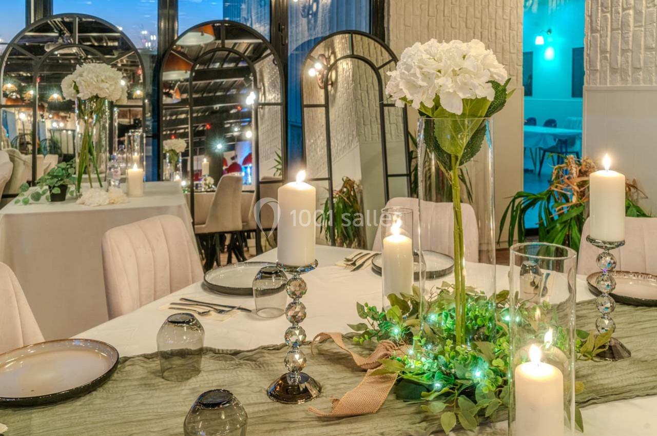 Table élégamment dressée avec bougies, fleurs blanches et décoration végétale dans un cadre lumineux et raffiné.