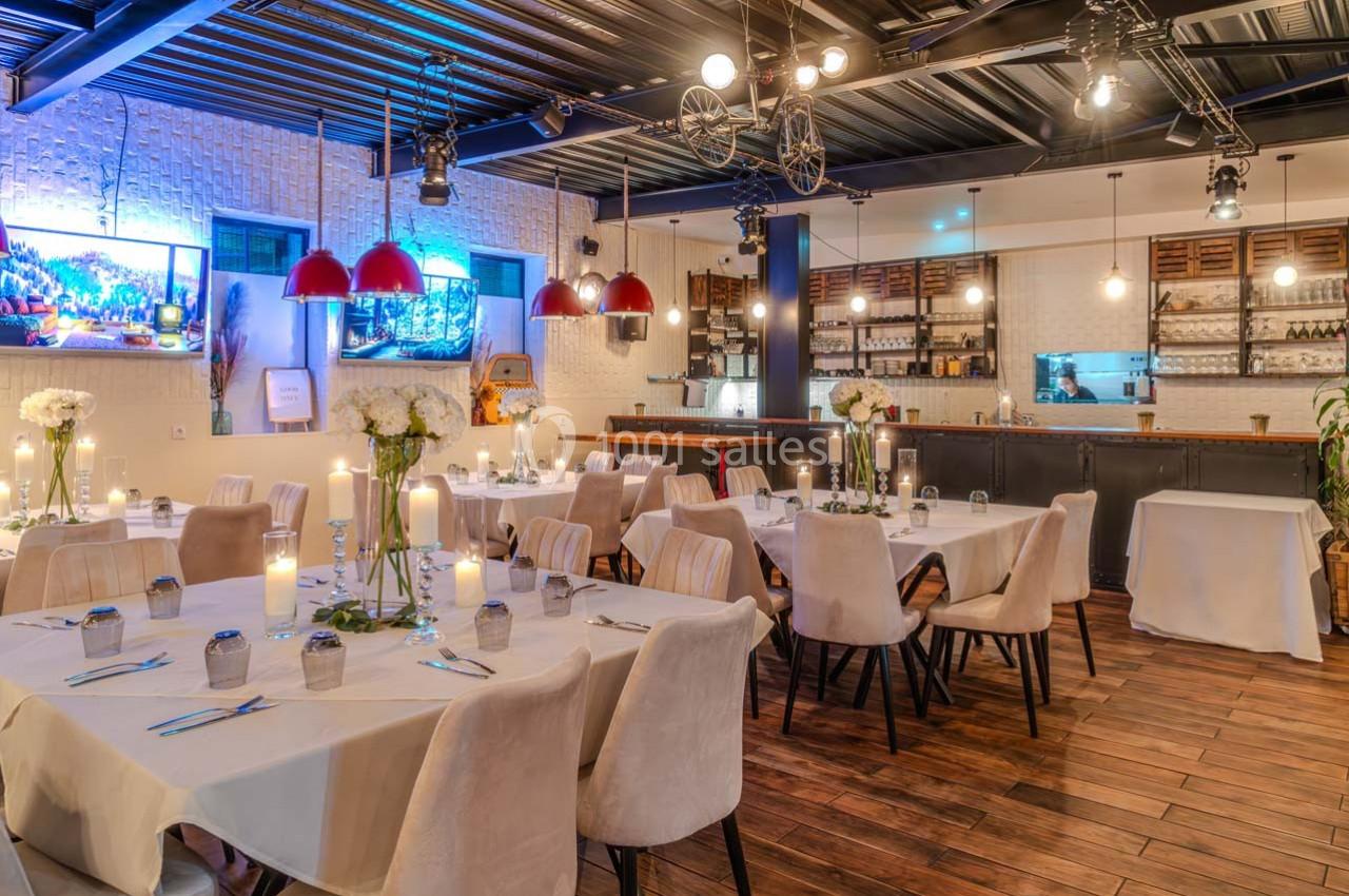 Salle de restaurant élégamment décorée avec des tables dressées, éclairage chaleureux et bar en arrière-plan.