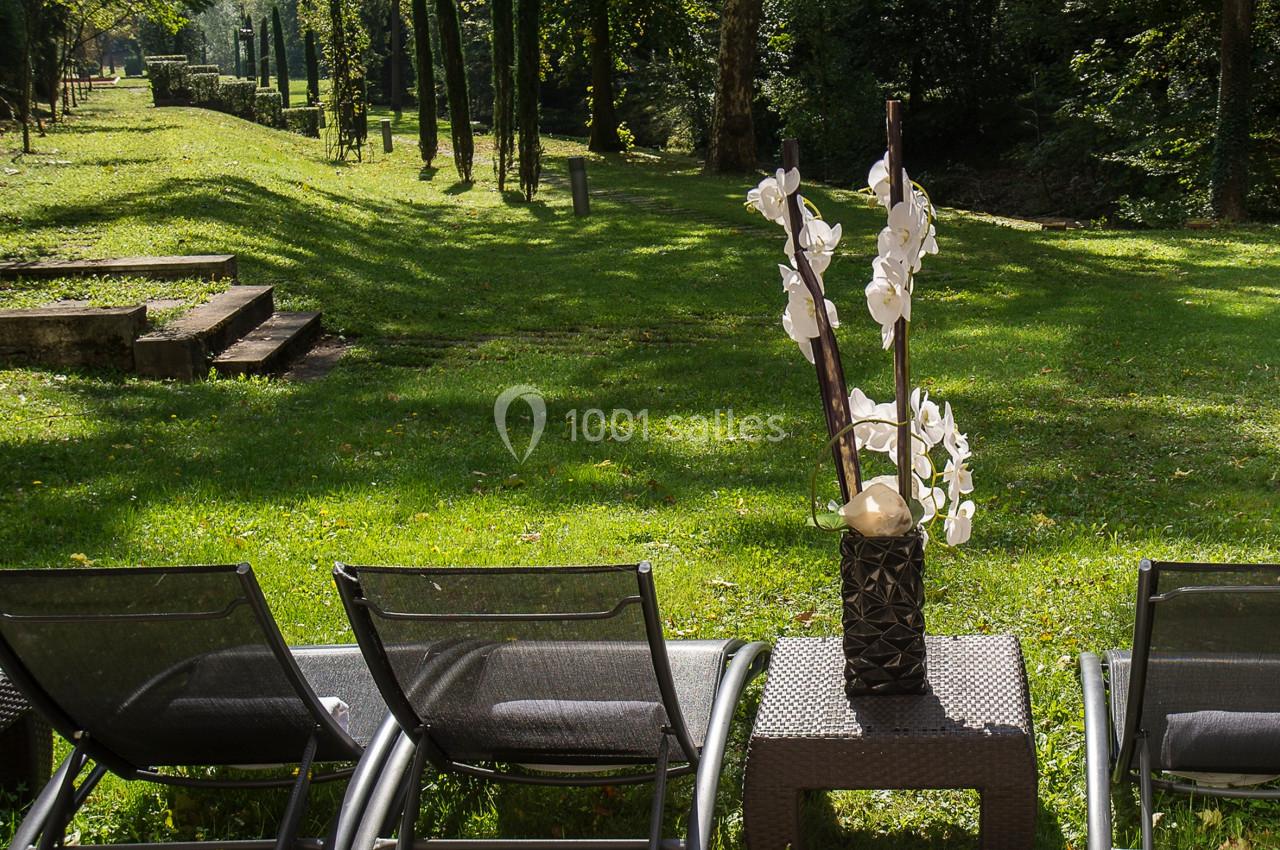 Chaises longues noires alignées sur une pelouse, avec un vase d'orchidées blanches posé sur une table basse.