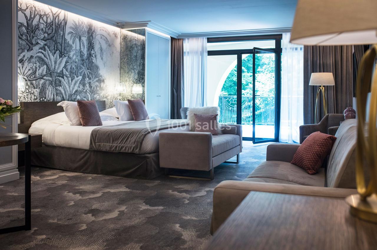 Chambre d'hôtel spacieuse avec lit double, canapé, décoration élégante et grande baie vitrée donnant sur un balcon.