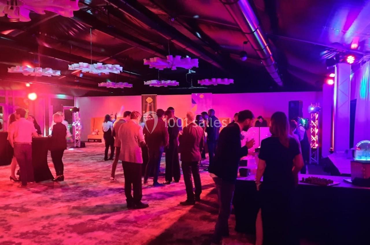 Groupe de personnes debout échangeant dans une salle éclairée par des lumières colorées lors d'un événement.