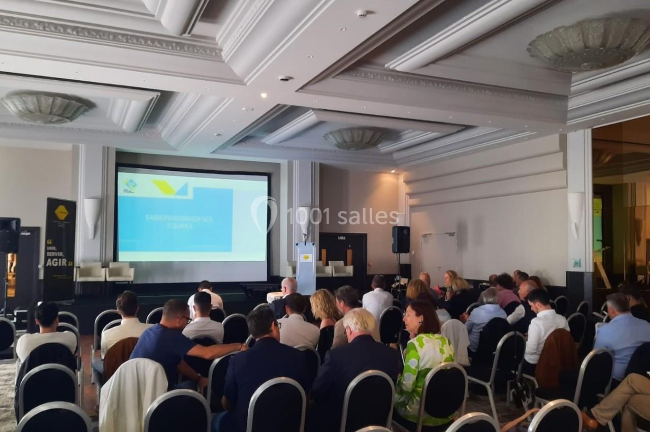 Salle de conférence avec des participants assis face à un écran de projection affichant une présentation.