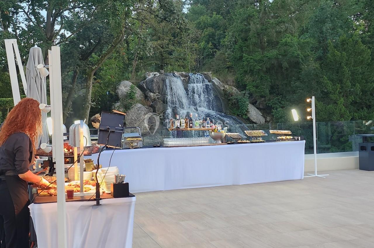 Buffet en plein air avec des tables garnies de plats, devant une cascade entourée de végétation.