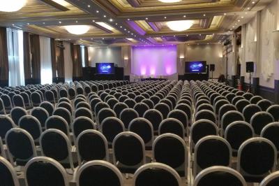 Un public assis dans une salle de conférence, attentif à une présentation sur une scène éclairée.