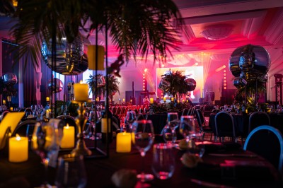 Des invités dînent autour de tables rondes tandis qu'un groupe joue sur une scène illuminée dans une salle de réception.