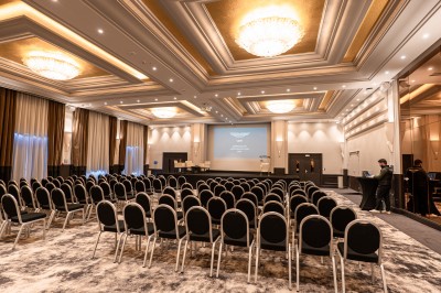 Des invités dînent autour de tables rondes tandis qu'un groupe joue sur une scène illuminée dans une salle de réception.