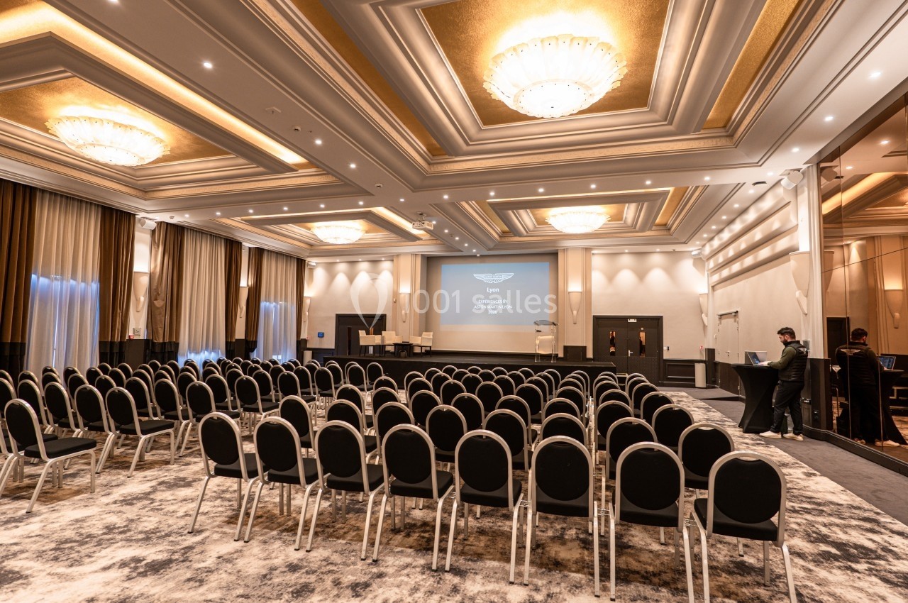 Salle de conférence élégante avec rangées de chaises noires, écran de projection allumé et éclairage raffiné.