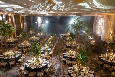 Des invités dînent autour de tables rondes tandis qu'un groupe joue sur une scène illuminée dans une salle de réception.