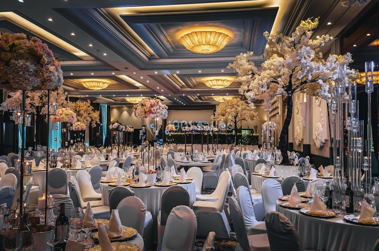 Salle de réception élégante avec tables rondes dressées, chaises blanches et décorations florales raffinées.