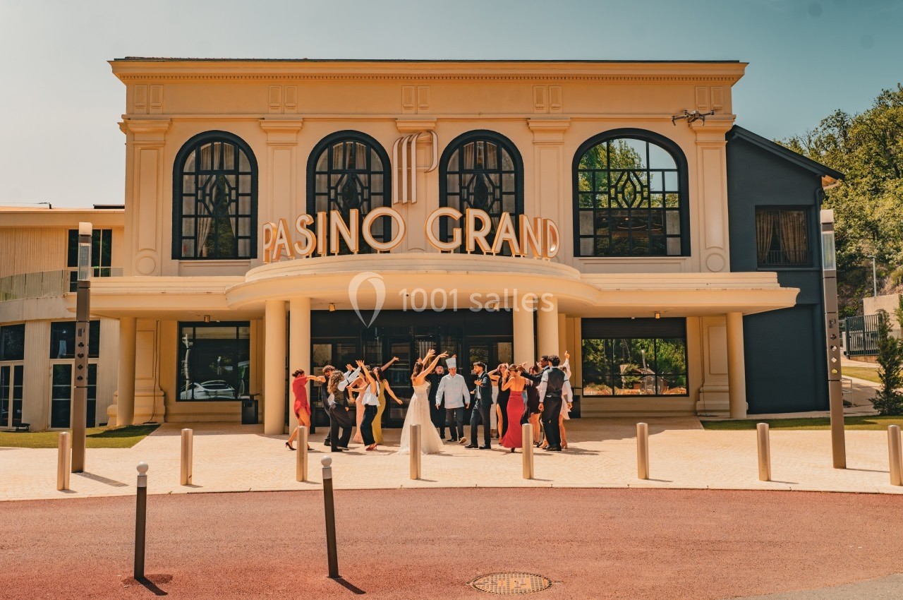 Groupe de personnes célébrant devant un bâtiment beige avec l'inscription ’Pasino Grand’ sur la façade.