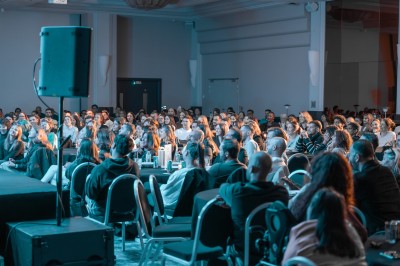 Des invités dînent autour de tables rondes tandis qu'un groupe joue sur une scène illuminée dans une salle de réception.