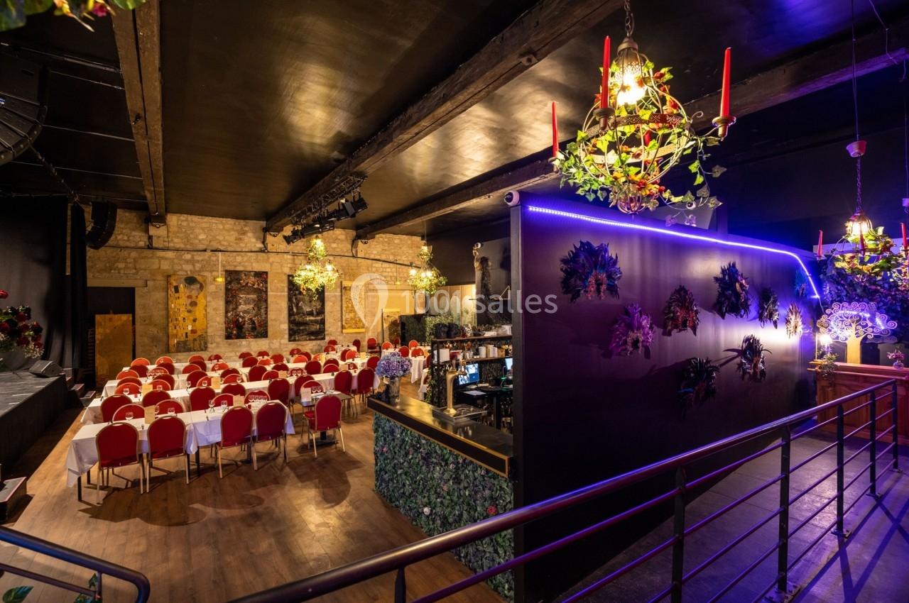 Salle de réception décorée avec des tables dressées, des chaises rouges, des lustres et des éléments végétaux.