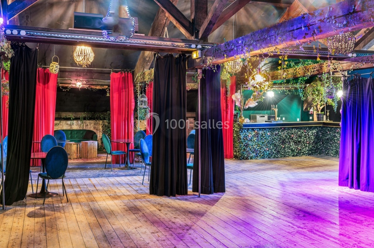 Salle spacieuse avec parquet en bois, rideaux rouges et noirs, mobilier élégant et bar décoré de plantes.
