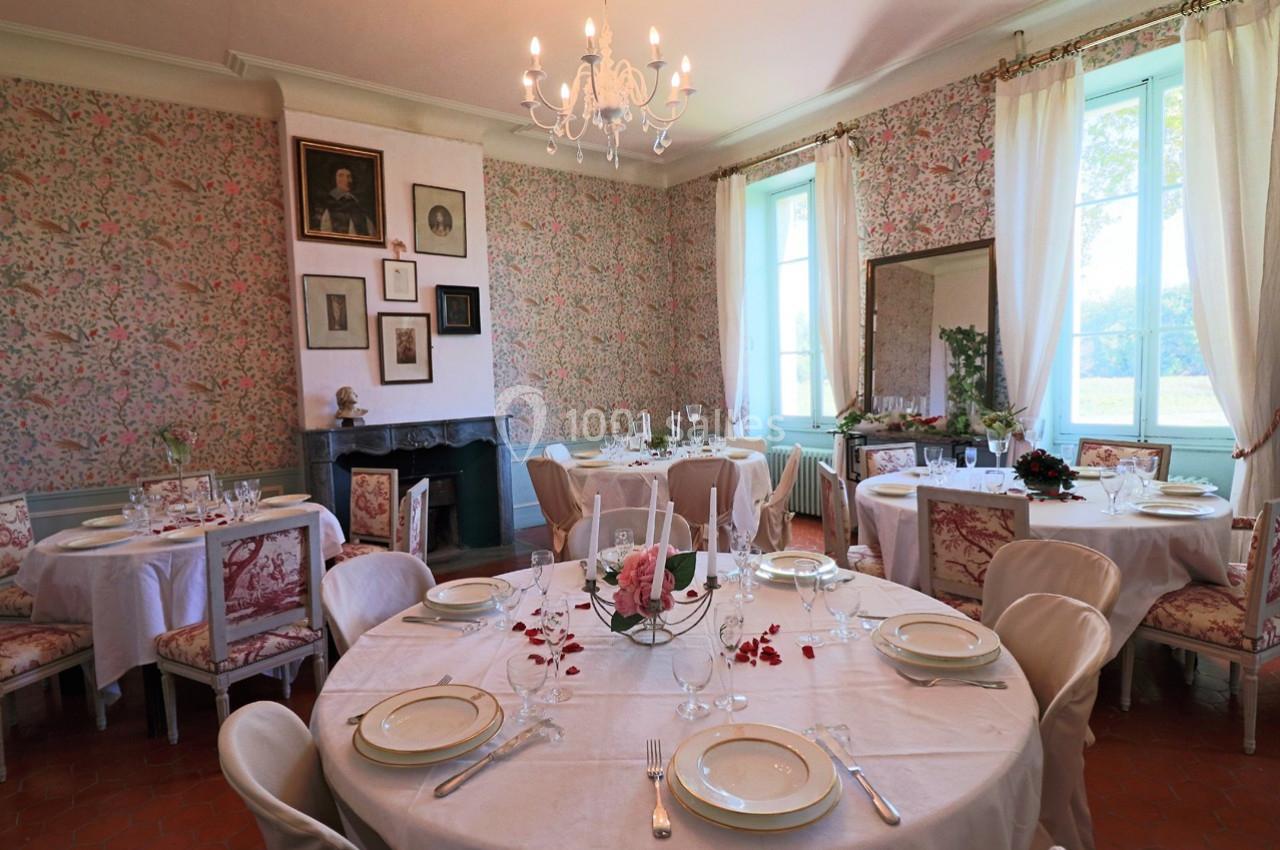 Salle à manger élégante avec tables rondes dressées, chaises tapissées, cheminée et murs décorés de papier peint fleuri.