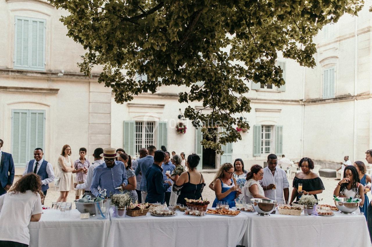 Groupe de personnes rassemblées autour d'une table dressée en extérieur, devant un bâtiment ancien.