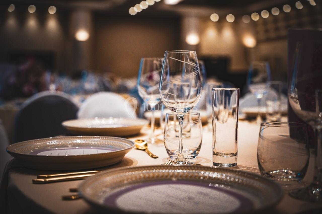 Location salle La Tour-de-Salvagny (Rhône) - Le Pasino Grand et l'Hôtel & Spa Le Pavillon #8 Table élégamment dressée avec assiettes, verres et couverts dorés dans une salle de réception éclairée.