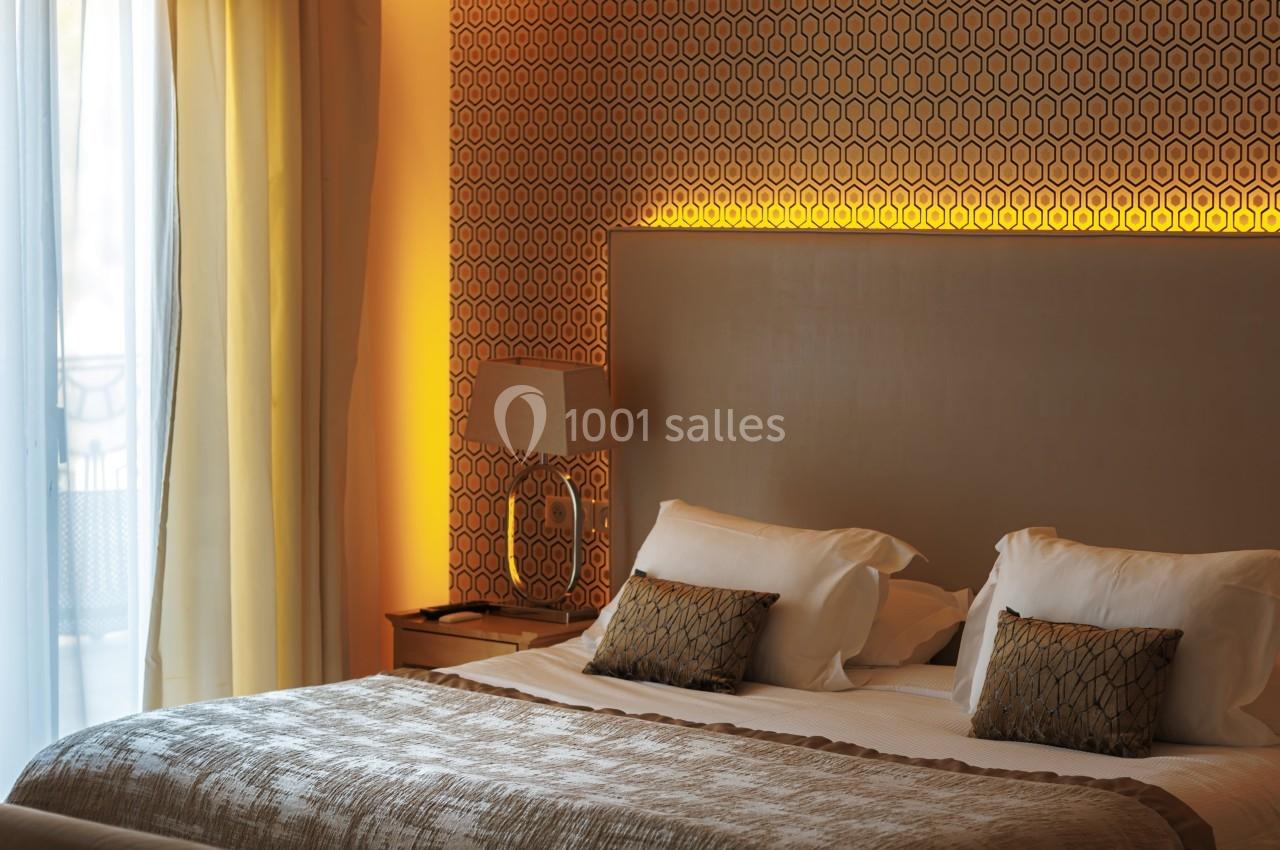 Location salle La Tour-de-Salvagny (Rhône) - Le Pasino Grand et l'Hôtel & Spa Le Pavillon #10 Lit double avec coussins décoratifs, lampe de chevet et éclairage tamisé, près d'une fenêtre avec rideaux clairs.
