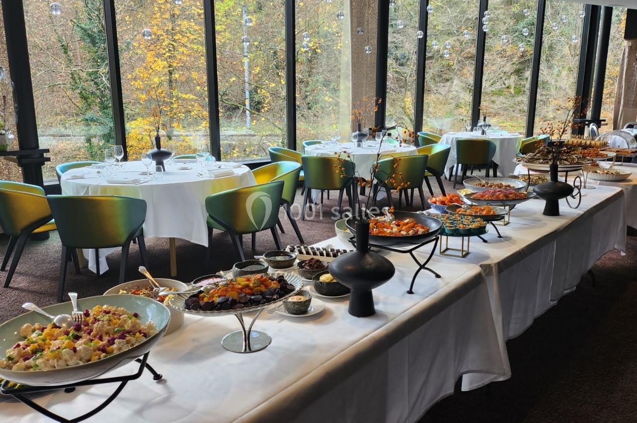 Buffet varié avec plats colorés dans une salle lumineuse, entourée de grandes baies vitrées donnant sur un paysage automnal.
