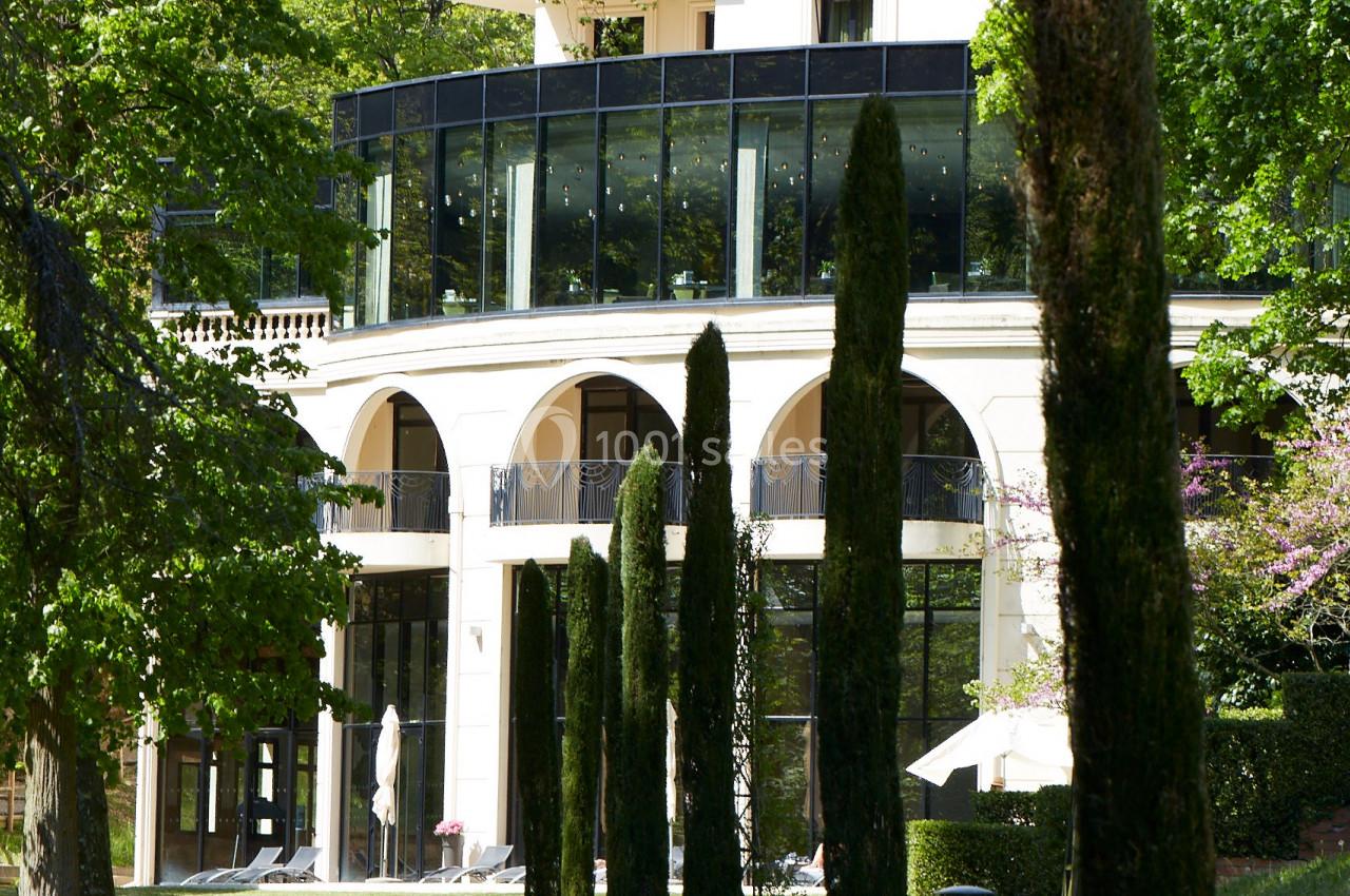 HOTEL*****&SPA LE PAVILLON Façade d'un bâtiment moderne entouré d'arbres et de cyprès, avec une pelouse au premier plan.