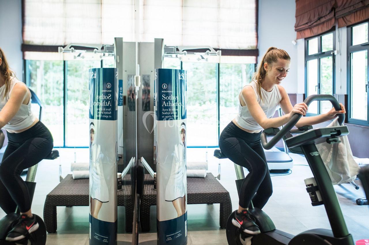 Salle de sport Une femme s'entraîne sur un vélo d'appartement dans une salle de sport lumineuse avec des miroirs.