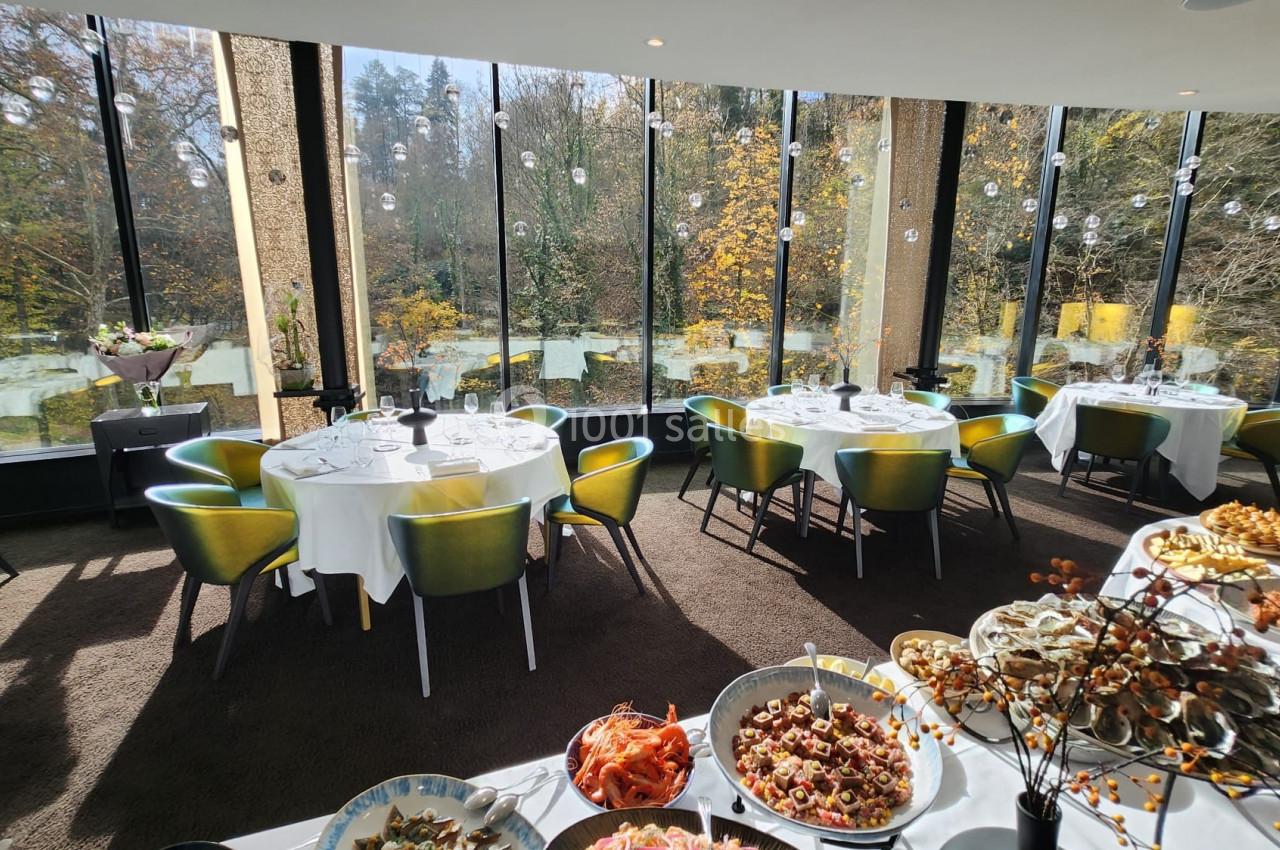 SALON DU PARC Salle de restaurant lumineuse avec de grandes baies vitrées donnant sur un paysage automnal, tables dressées et buffet.