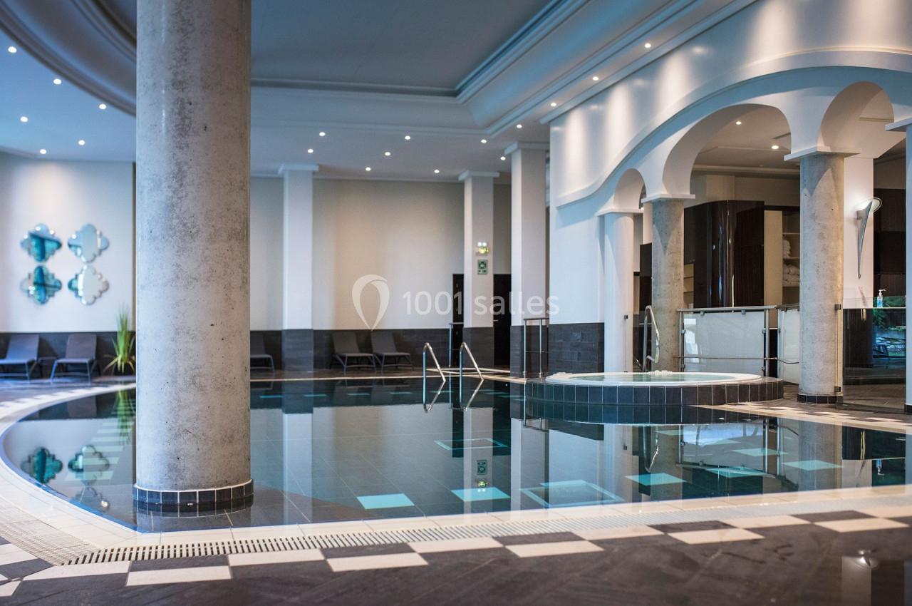 SPA Piscine intérieure moderne avec colonnes, chaises longues et éclairage tamisé dans un espace élégant.