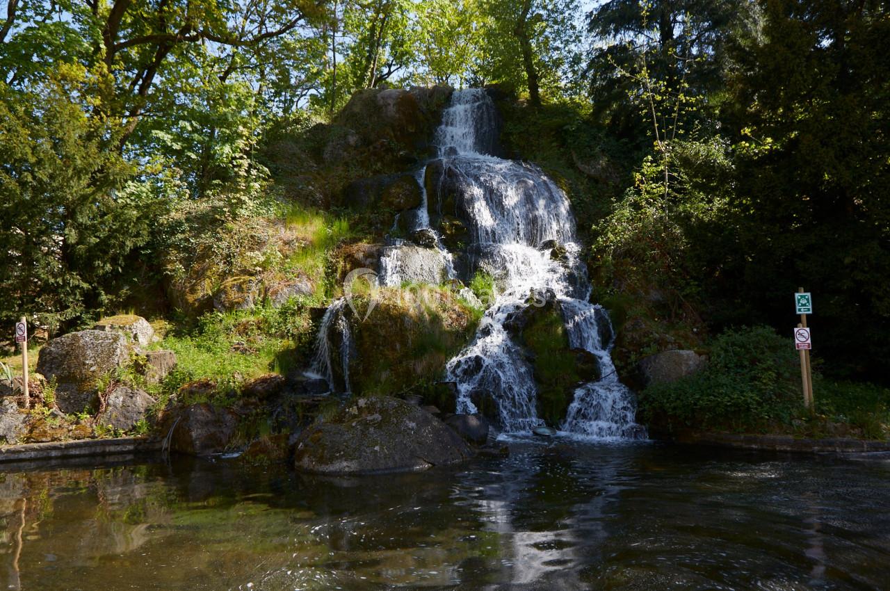 Vue de la terrasse Cascade naturelle entourée de végétation, se déversant dans un bassin calme sous une lumière ensoleillée.