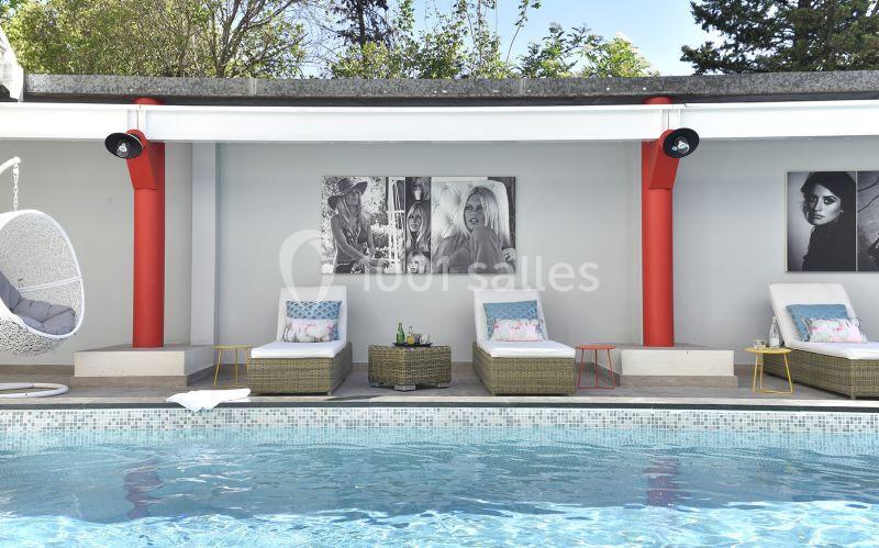 Chaises longues et table basse près d'une piscine, avec des photos en noir et blanc accrochées sur un mur clair.