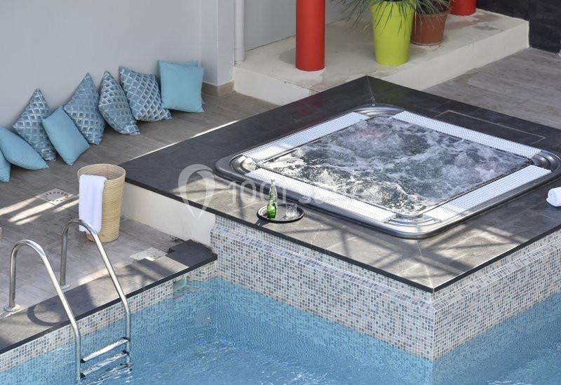 Jacuzzi en fonctionnement près d'une piscine, entouré de coussins et de plantes dans un espace extérieur moderne.