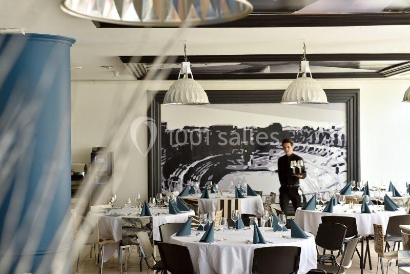 Salle de restaurant élégante avec tables dressées de nappes blanches et serviettes pliées, un serveur en arrière-plan.